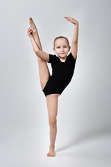 little gymnast demonstrates flexibility and balance in a gymnastic pose by lifting her leg