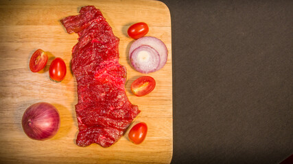 Fresh meats, vegetables and spices are laid out on a food prep table covered with a black tablecloth..