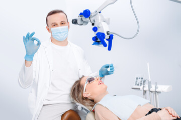 A male dentist in mask and a patient woman in the dentist chair. Male dentist examining patient looking on the teeth with professional microscope at surgery dental office.