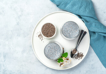 Two portions of chia seed pudding and coconut milk on a flat plate with a flower on a gray background. Top view, horizontal.