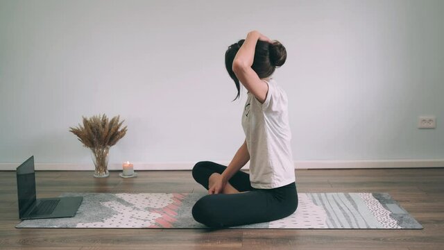 Caucasian woman does yoga online A woman sits in a lotus position and stretches her neck with her hands Yoga for beginners Gymnastics Classes Funny yoga Side view