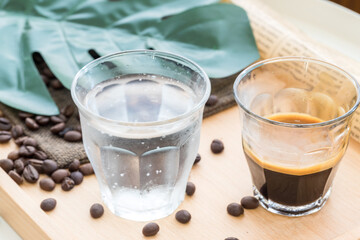 Espresso shot in glass place near coffee bean pile. International famous aroma beverage. Cup of coffee on an old wooden table.