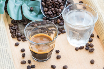 Espresso shot in glass place near coffee bean pile. International famous aroma beverage. Cup of coffee on an old wooden table.