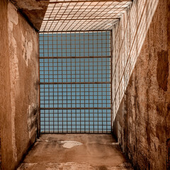 Looking up through a rustic stone structure, a grid filters the expansive blue sky above. Discover new perspectives.