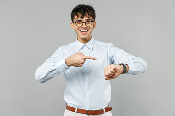 Young smiling successful employee business latin man 20s wearing corporate lawyer wear classic white shirt glasses point index finger on smart watch isolated on grey color background studio portrait