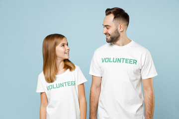 Obraz premium Two friends couple teen girl man wears white t-shirt green title volunteer look to each other isolated on pastel blue color background. Voluntary free team work assistance help charity grace concept.