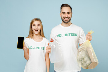 Two young couple teen girl man wears white t-shirt green title volunteer hold bag trash use mobile phone isolated on pastel blue color background. Voluntary free team work help charity grace concept.