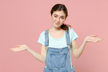 Young confused mistaken uncertain doubtful expresive caucasian woman in denim clothes blue tshirt spread hands oops gesture isolated on pastel pink background studio portrait People lifestyle concept