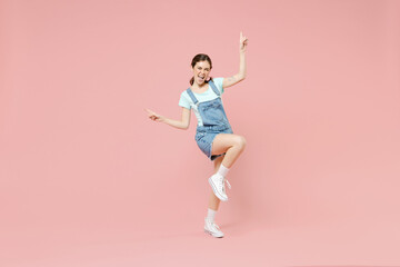 Fototapeta na wymiar Full length young overjoyed happy caucasian woman in trendy denim clothes blue tshirt do winner gesture point index fingers up raise up leg isolated on pastel pink background People lifestyle concept