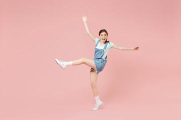 Fototapeta na wymiar Full length young smiling joyful caucasian woman 20s in trendy denim clothes blue tshirt stand on toes dancing with outstretched hands raised up leg isolated on pastel pink background studio portrait