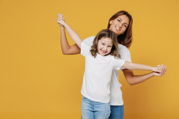 Happy woman in basic white t-shirt have fun dance cute child baby girl 5-6 years old. Mommy mum little kid daughter isolated on yellow orange color background studio. Mother's Day love family concept.