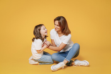 Full body length happy woman in basic white t-shirt have fun sit on floor with child baby girl 5-6 year old Mom little kid daughter isolated on yellow color background studio Mother's Day love family