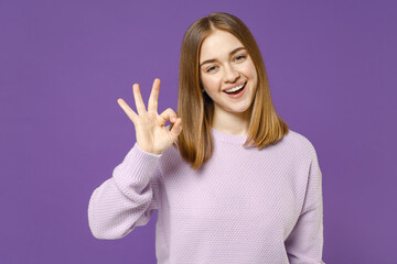 Young smiling fun positive happy cheerful student caucasian woman 20s wearing purple knitted sweater show ok okay gesture isolated on violet color background studio portrait People lifestyle concept.