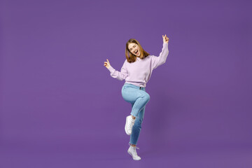 Full length young overjoyed happy student caucasian woman in purple sweater do winner gesture point finger up with raised up leg isolated on violet background studio portrait People lifestyle concept.