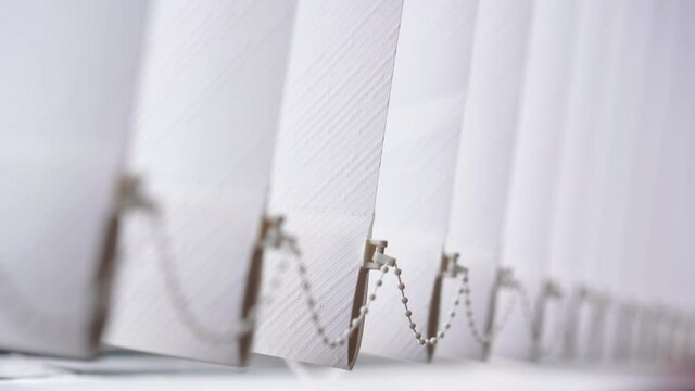 Big vertical modern venetian blind hangs on window in office room