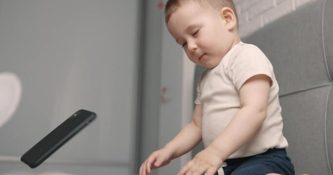 Little angry boy with a mobile phone in his hands whims and throws smartphone. Slow motion