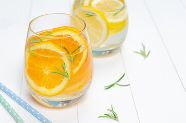 Preparation of the lemonade drink and orange juice Lemonade in the jug and lemons with rosemary on the table outdoor.