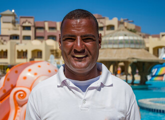 Portrait of a smiling Egyptian man 40 years old in a white T-shirt on the background of the resort landscape.