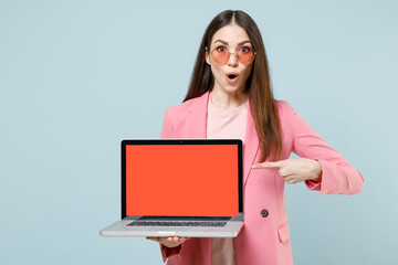 Young shocked confused woman in pastel pink clothes glasses point index finger on laptop pc...