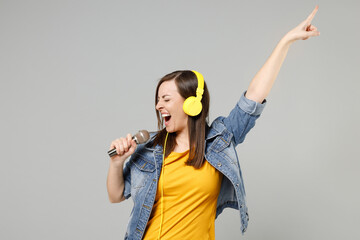 Young fun caucasian expressive woman 20s wearing casual trendy denim jacket yellow t-shirt headphones sing song in microphone point index finger up isolated on grey color background studio portrait