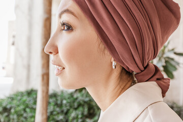 A woman in an unusual red turban with an earring poses in an Arab city