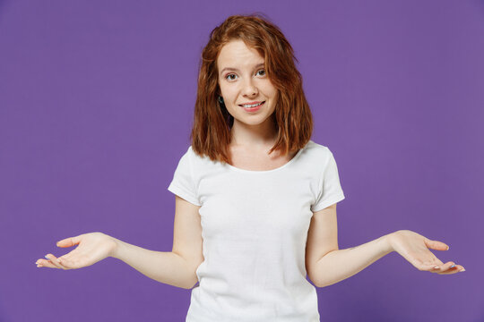 Young sad uncertain mistaken doubtful ashamed confused caucasian woman 20s wearing white basic casual t-shirt spreading hands oops gesture isolated on dark violet color background studio portrait