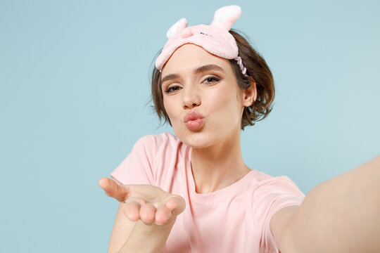 Close up young woman in pajamas jam sleep eye mask rest relaxing at home do selfie shot mobile phone blow air kiss isolated on pastel blue background studio portrait. Good mood night bedtime concept.
