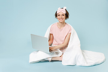 Young woman in pajamas jam sleep eye mask rest home sit wrap cover under blanket duvet hold laptop...