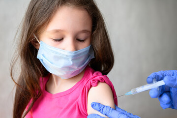 Vaccination of kid from COVID-19 or flu, cute little girl in mask closes eyes during injection