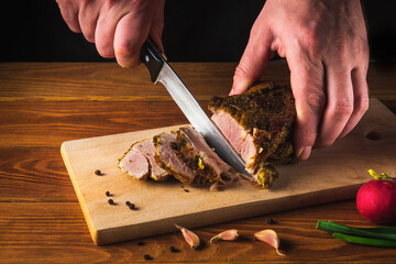 Chef hands slicing baked beef steak with knife on wood cutting desk. Top view food preparation process concept