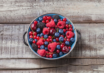 Berries assorted fresh mix ready to eat kitchen arrangement in rustic old blue metal plate on old kitchen wooden table overhead studio shot