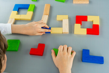 Boy's hand with a wooden cube on the gray background. Multi-colored cubes on the table. Geometric shapes on a wooden background. Puzzle concept.