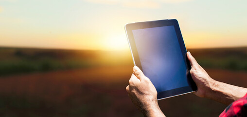 Farmer with tablet computer on the plantation field countryside at sunset. Space for text.