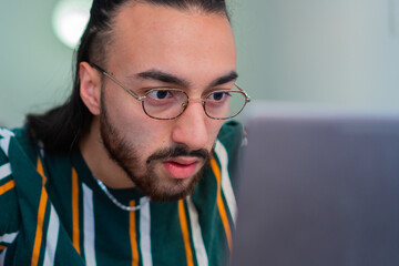 young latin long-haired man in shock as he looks at his computer, wearing glasses