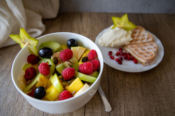 White bowl of fresh healthy fruit salad on wooden background with carambola star