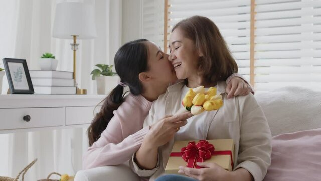 Attractive Beautiful Asian Middle Age Mum Sit With Grown Up Daughter Give Gift Box And Flower In Family Moment Celebrate Mother Day. Overjoy Bonding Cheerful Kid Embrace Relationship With Retired Mom.