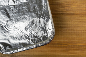 Tray with meal wrapped in aluminum foil for baking in the oven. Aluminum foil texture close up.