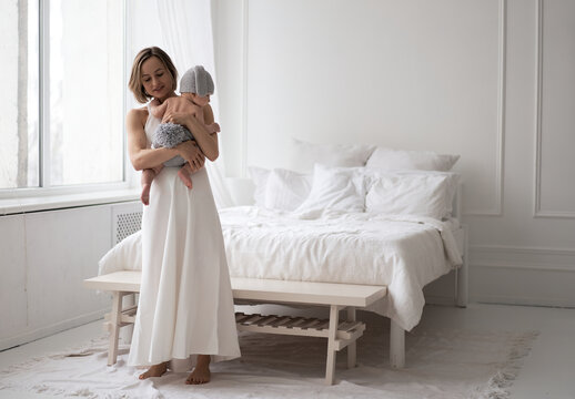 Mother in white dress holding a baby boy in a bunny costume and play with him. High quality photo