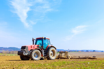 A farmer plows the soil in the field with a chisel plow on a tractor. Agricultural tractor with a plow on farmland.