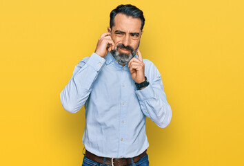 Middle aged man with beard wearing business shirt covering ears with fingers with annoyed...