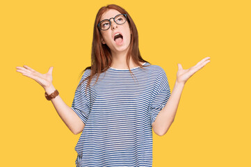 Young read head woman wearing casual clothes and glasses crazy and mad shouting and yelling with...