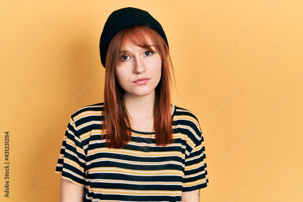 Poster redhead young woman wearing wool cap with serious expression on face. simple and natural looking at 