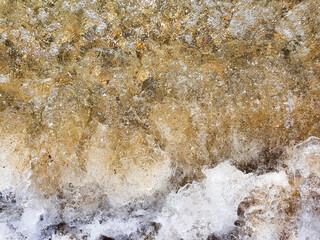 Sea wave mixes with sand, sea foam, water splash. Top view. Beach sunset abstract background.