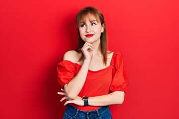 Redhead young woman wearing casual red t shirt with hand on chin thinking about question, pensive expression. smiling and thoughtful face. doubt concept.