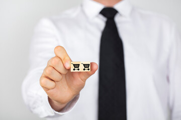 Businessman shows a wooden cube with shopping cart icon. Online shopping or add to basket concept.