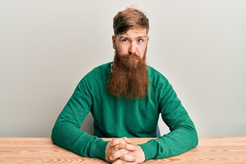 Young irish redhead man wearing casual clothes sitting on the table skeptic and nervous, frowning...