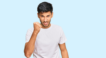 Young handsome man wearing casual white tshirt angry and mad raising fist frustrated and furious while shouting with anger. rage and aggressive concept.