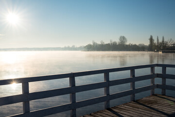 Jetty on a lake with fog. Wooden structure on the water. Sunrise and fog over the water.