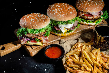 Set of delicious grilled burgers with beef, tomatoes, cheese, cucumber, lettuce, french fries, sauce on a dark background. The concept of food meal