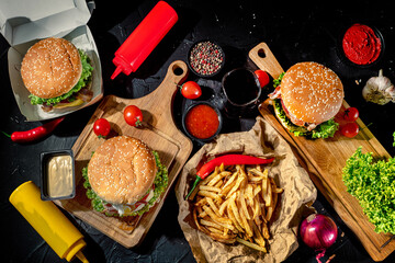 Fototapeta na wymiar Set of delicious grilled burgers with beef, tomatoes, cheese, cucumber, lettuce, french fries, sauce on a dark background. Top view with copy space. The concept of food meal